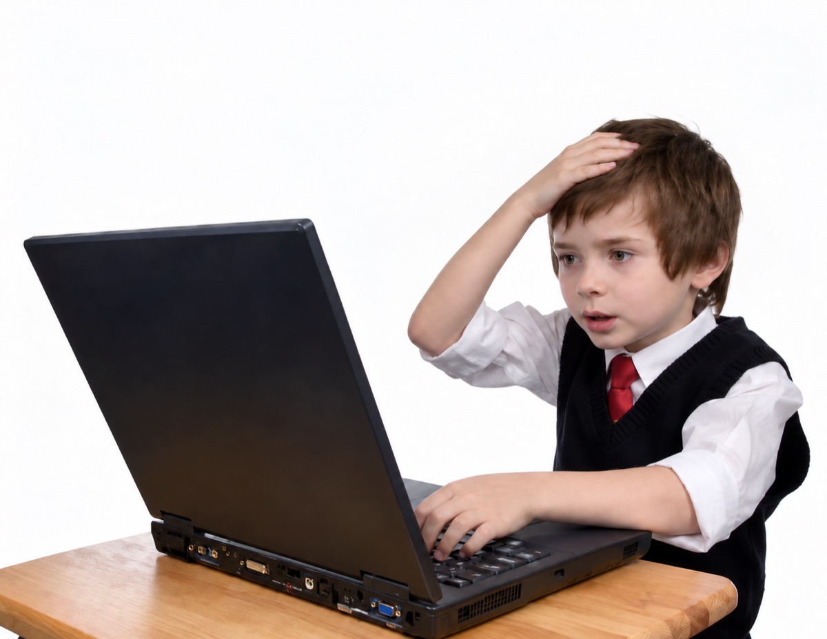 A boy at a laptop with a hand on his head, looking overwhelmed